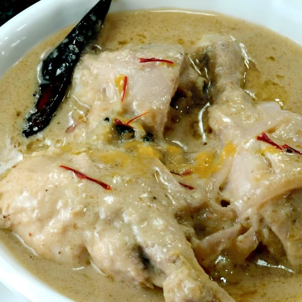 Creamy chicken curry with red chili and saffron threads in a white bowl.