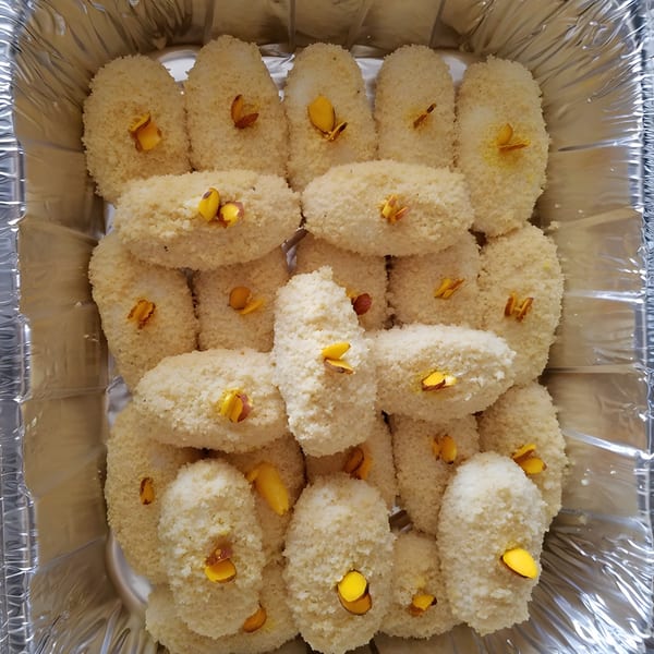 Close-up of Rakhi's Kitchen's coconut barfi, garnished with yellow almond slivers in a foil tray.