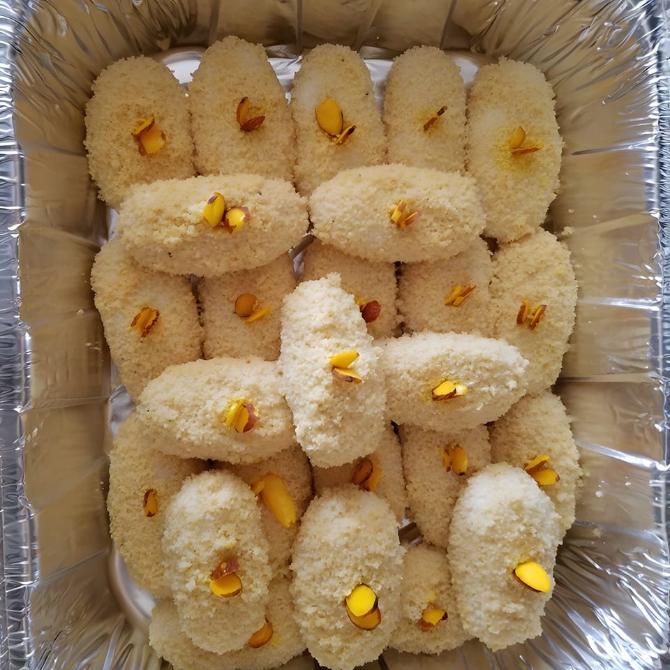 Close-up of Rakhi's Kitchen's coconut barfi, garnished with yellow almond slivers in a foil tray.