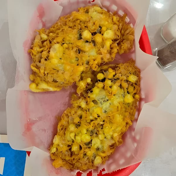 Two golden-brown corn fritters in a red basket lined with white paper, with salt and pepper shakers nearby.