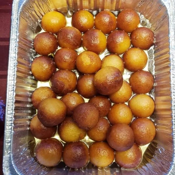 A foil tray filled with many golden-brown gulab jamun, soaked in syrup, from Rakhi's Kitchen.