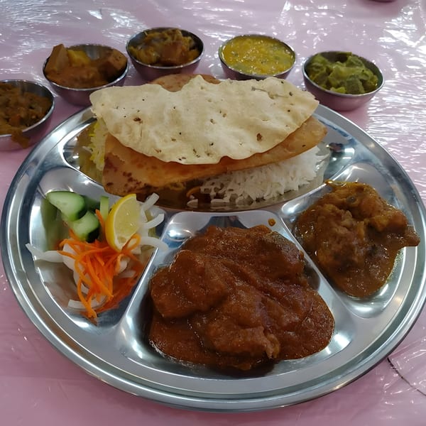 A Rakhi's Kitchen fast-food thali with rice, curries, flatbread, and salad on a metal plate.