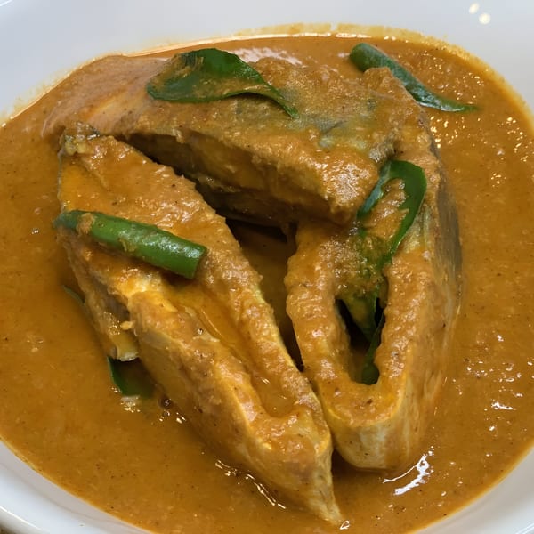 Close-up of Rakhi's Kitchen's fish curry, featuring fish steaks in a rich orange sauce with green garnishes.